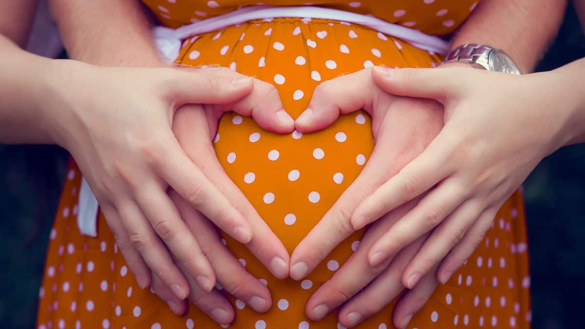 Pregnant woman with mans hand shaped as heart